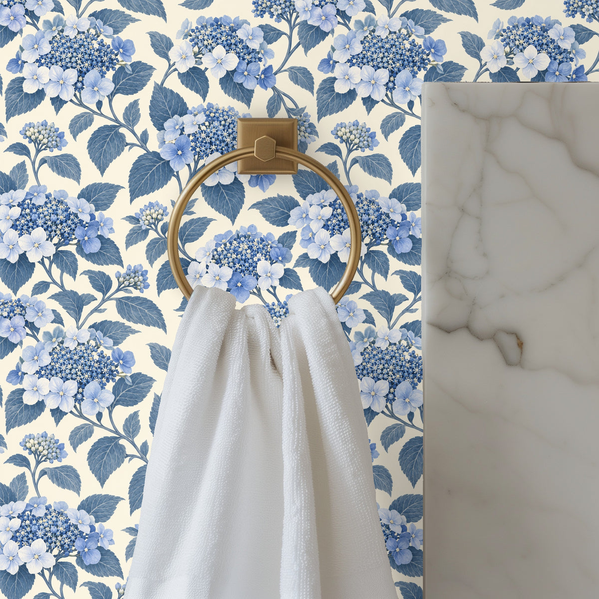 Bathroom vignette showing brass towel ring and marble counter in front of blue hydrangea wallpaper