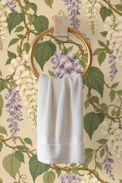 Close-up of creamy wisteria flowers and green leaves against a beige wall.