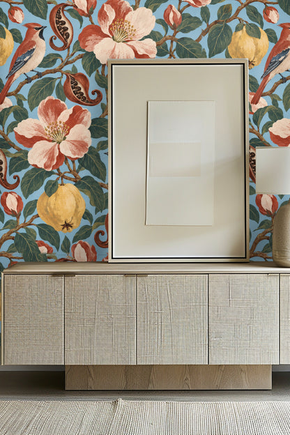 Close-up of wallpaper featuring quinces, waxwing birds, pomegranate seeds and large terracotta-pink flowers on a sky blue background
