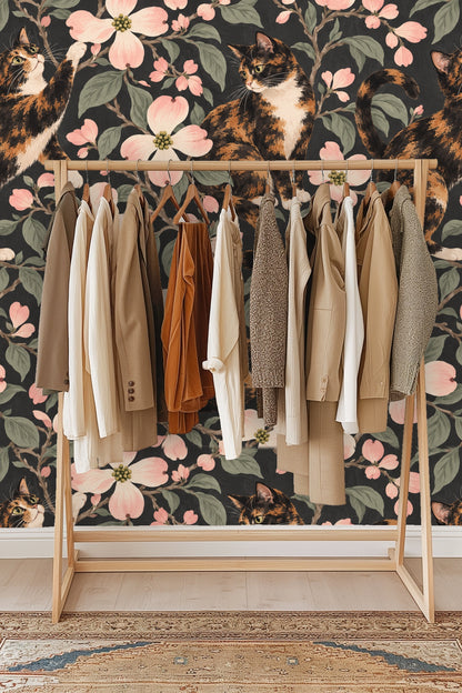 Side profile of a calico cat sitting among dogwood blossoms on patterned wallpaper.