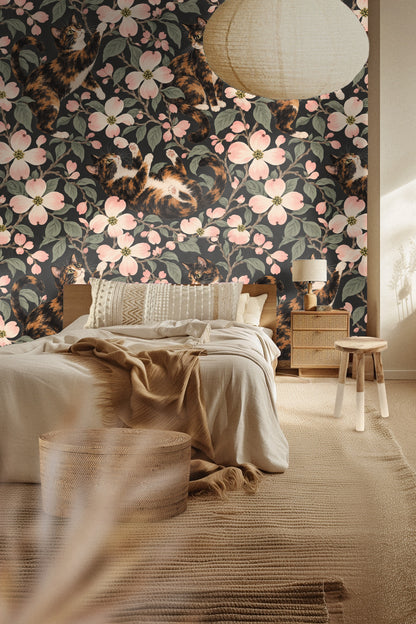 Calico cat reaching upward among pink dogwood blossoms on wallpaper.