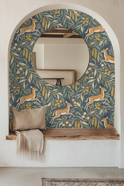 Blue velvet sofa in front of the Impala Leaf Procession wallpaper with ochre and green leaf motifs