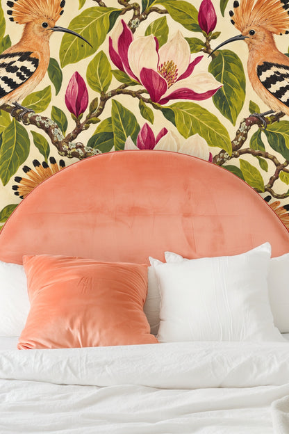 Hand placing a swatch of Hoopoe Magnolia Chorus wallpaper with bird and magnolia flower motif, illustrating scale and color detail.