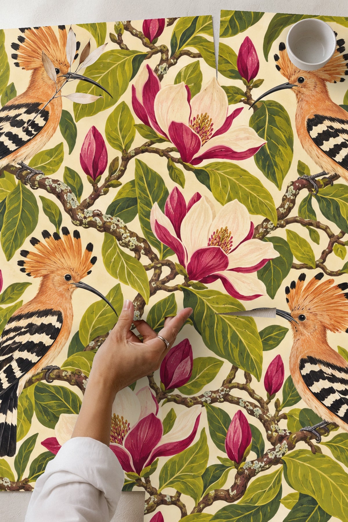 Close-up image of a living room with Hoopoe Magnolia Chorus wallpaper showing detailed birds and floral pattern behind a sofa and table.