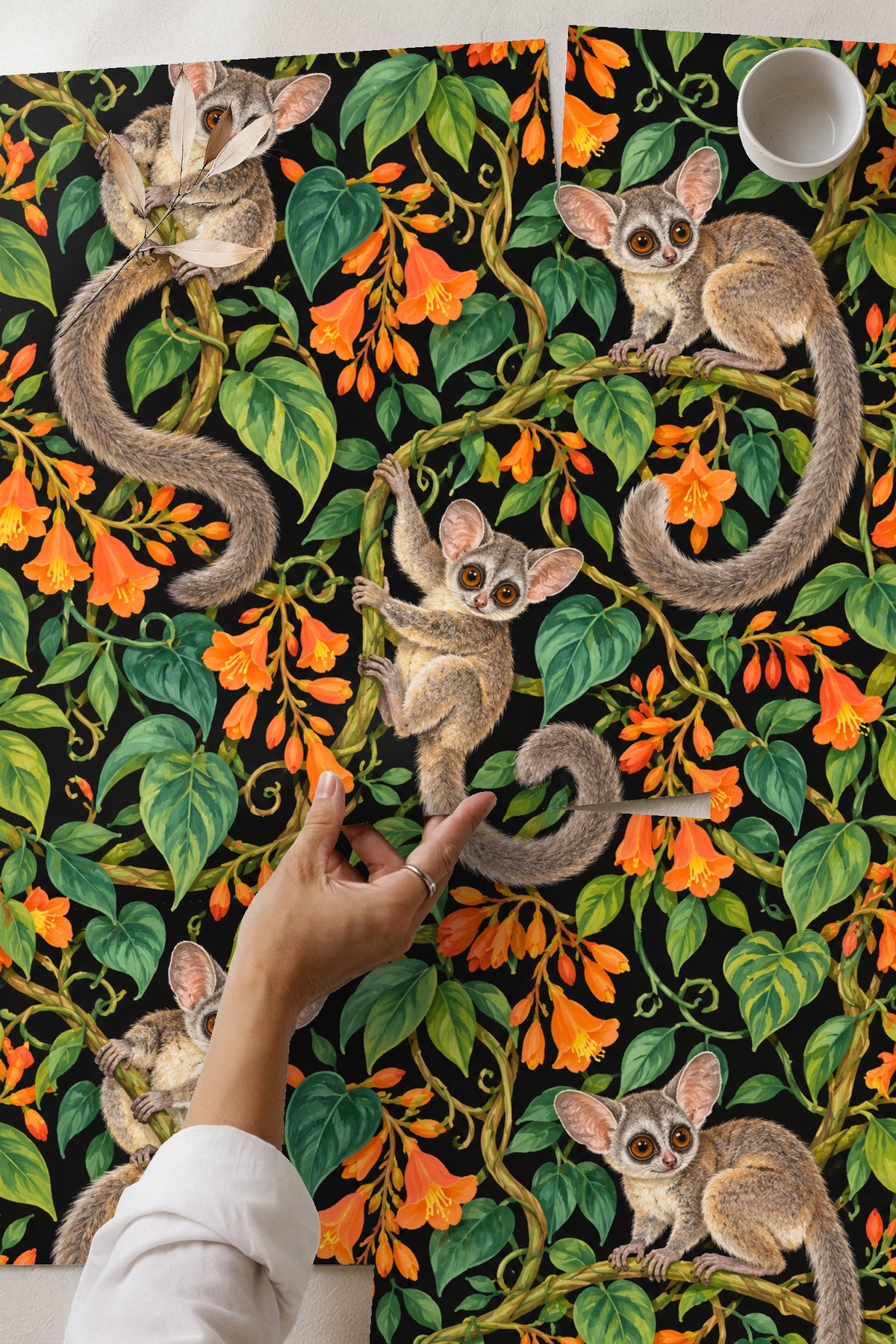 Close-up of two galagos clinging to intertwined vines with vivid orange trumpet flowers on black ground.