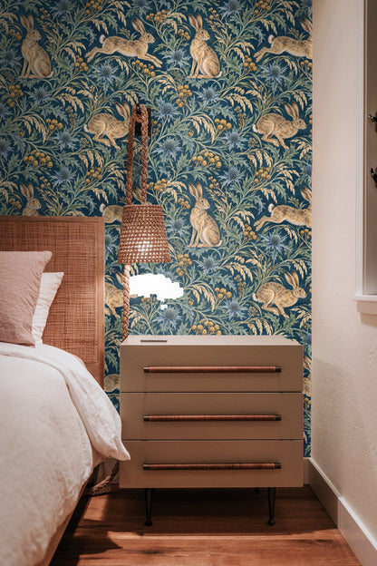 Living room interior with Sea Holly & Harewind wallpaper behind a cream armchair and small wooden side table