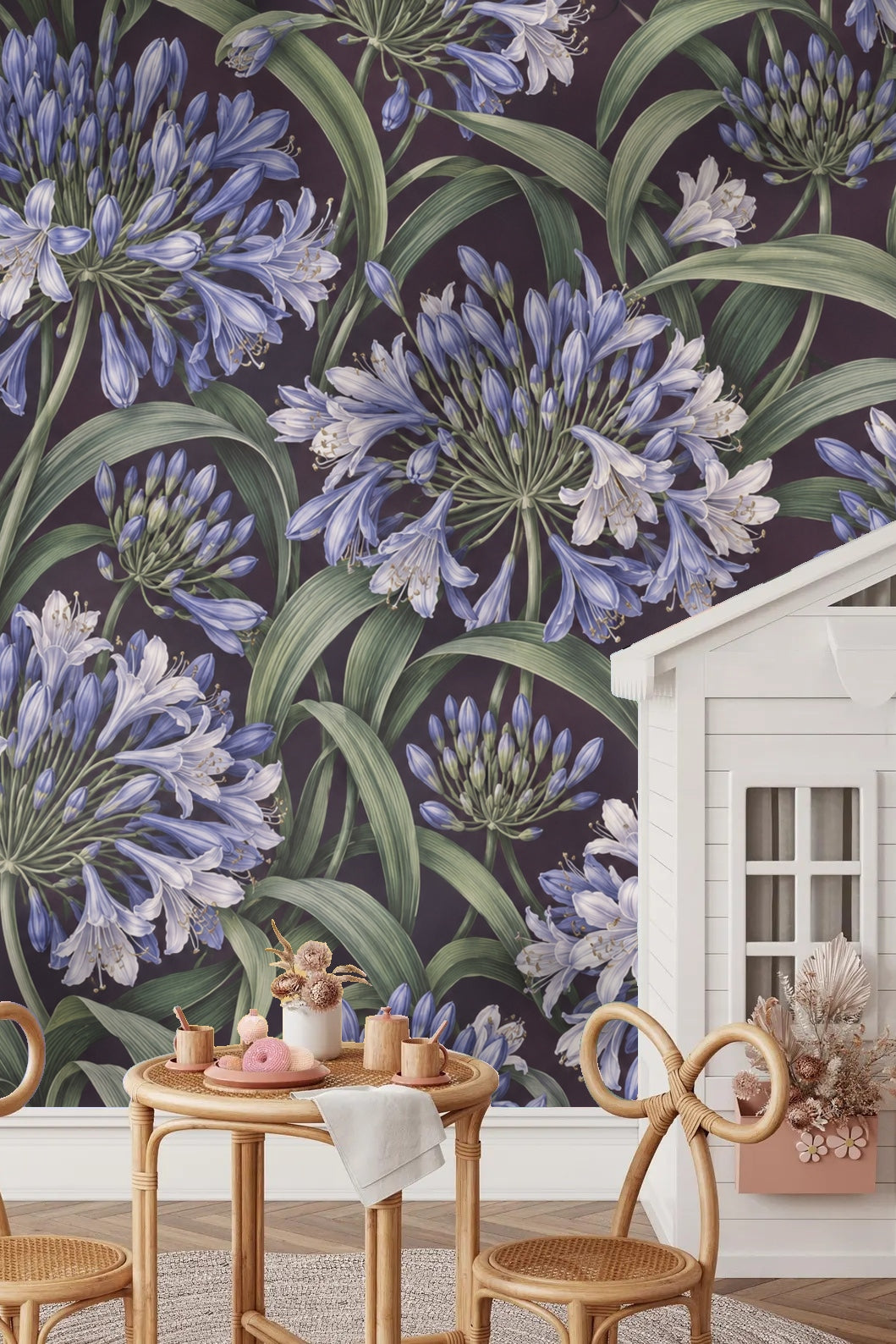 Bedroom scene with rattan bedframe and Agapanthus Rainwheel wallpaper as a backdrop behind pillows in blue and cream.