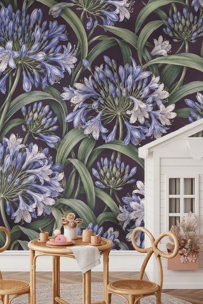 Bedroom scene with rattan bedframe and Agapanthus Rainwheel wallpaper as a backdrop behind pillows in blue and cream.