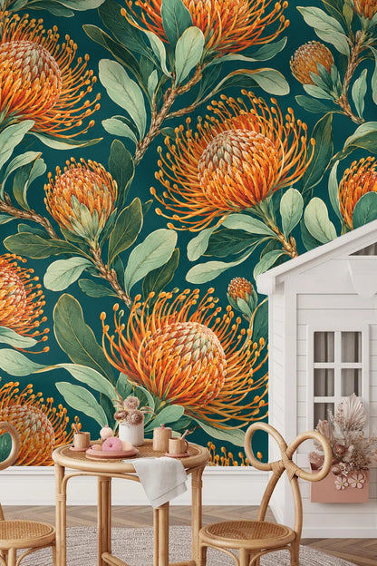 Dining room wall featuring large-scale pincushion protea wallpaper with orange flowers and green foliage behind a wooden table and gold-fram