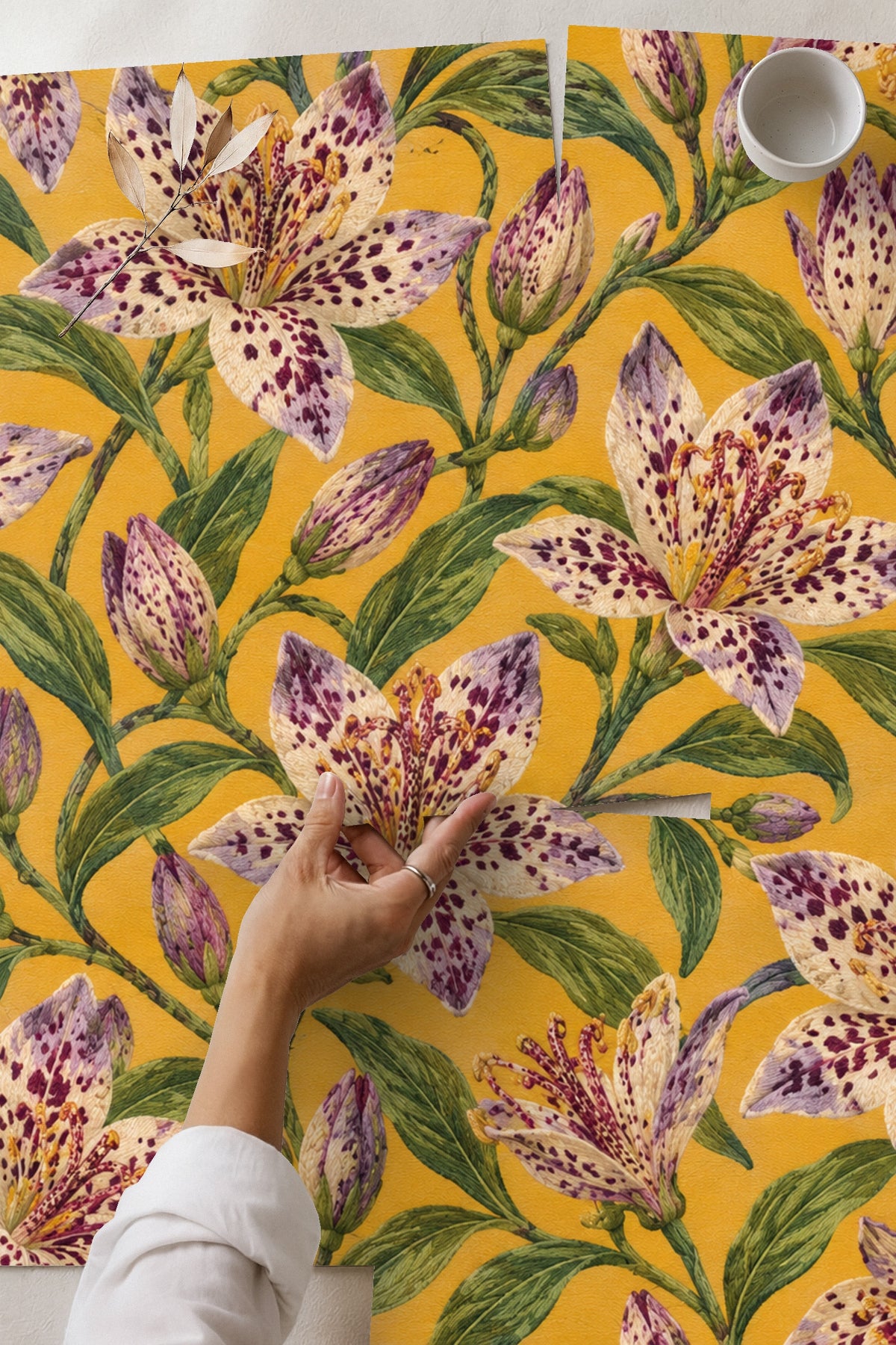 Bedroom wall decorated with Tricyrtis Speckled Rhapsody wallpaper behind bed, showing botanical floral pattern with purple spotted lilies on