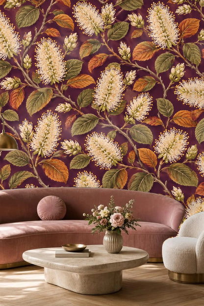 Living room with a bold wallpaper of ivory bottlebrush flowers and autumnal leaves on plum behind an orange sofa and mid-century style decor