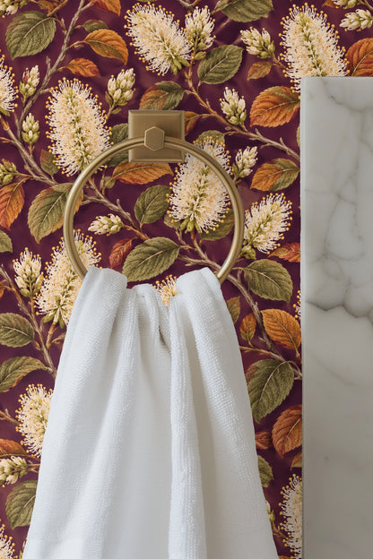 Close-up of cream colored bottlebrush flowers and textured olive and rust leaves on dark plum wall