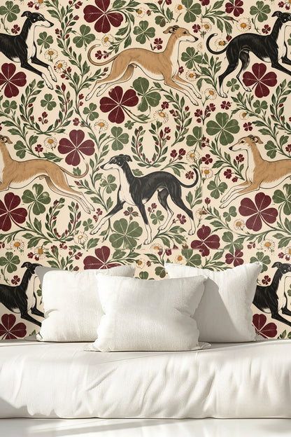 Close-up of black greyhound standing amidst illustrated clover leaves and flowers on wallpaper.