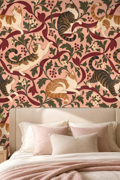 Wallpaper pattern with tabby cats playing and climbing around flowing crimson ribbons and green leaves on mauve pink background.