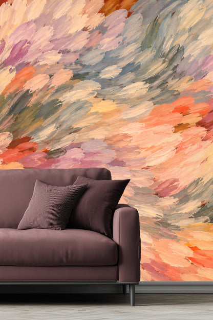 Close-up of an entryway wall under stairs featuring artistic brushstroke wallpaper in warm pastel tones with a wooden console table and lamp