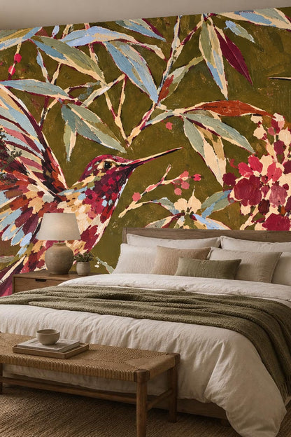 Bedroom decorated with painterly floral and hummingbird wallpaper mural in olive green and crimson hues behind bed with earth-toned bedding