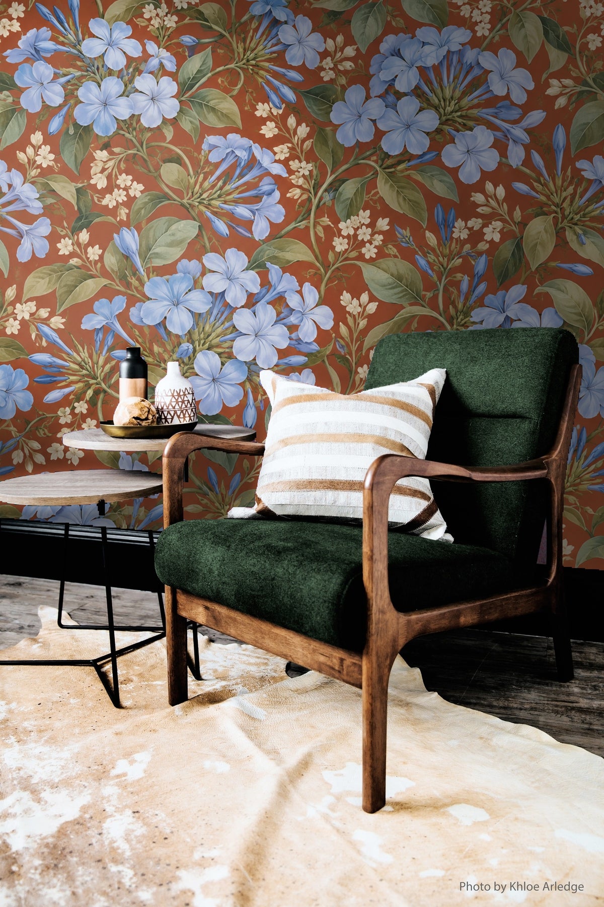 Close-up of hand holding wallpaper sample featuring blue plumbago clusters on terracotta background