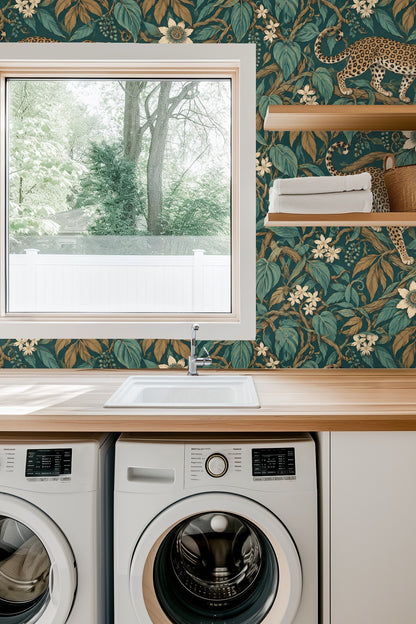 Interior shot showing Jungle Jaguar Parade wallpaper behind a blue velvet sofa, highlighting the rich teal and ochre botanical pattern.