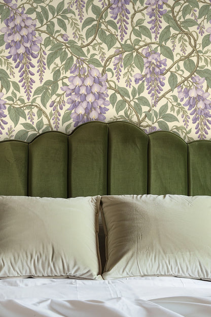 Close-up of Wisteria Cascade wallpaper with a lit cream candle and glass vase holding white baby's breath flowers on a wooden surface