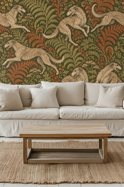 Bedroom wall with Woodland Whippet Chase wallpaper behind green velvet headboard and cream pillows.