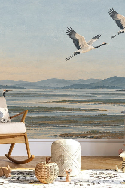 Child's room with rocking chair and pouf in front of the cranes wallpaper mural.