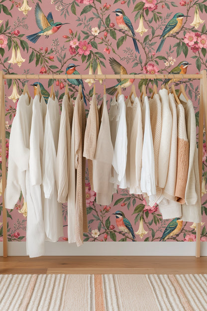 Detail of flying hummingbird with soft pink flower buds and green foliage on dusty rose wallpaper