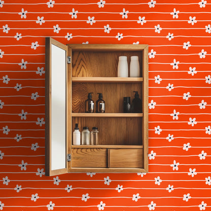 Repeat pattern swatch: bright clementine-orange field with irregular cream horizontal lines and pale five-petal daisies with charcoal dots.