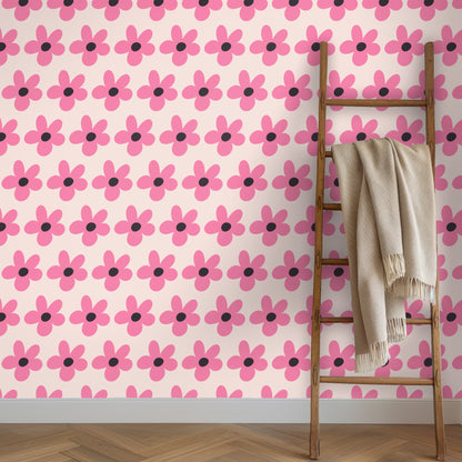 Close-up of the wallpaper pattern showing bold five-petal pink flowers with charcoal centers on a pale blush background