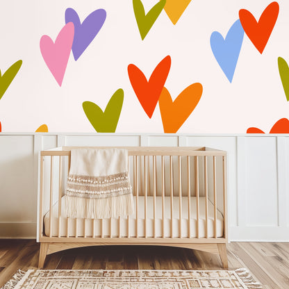 Nursery scene with a simple wooden crib placed in front of the oversized heart wallpaper in warm, playful colors