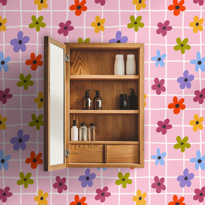Close-up of Prima Bloom Grid wallpaper showing a blush pink field, irregular cream grid lines and multicolored five‑petal flowers with dark‑