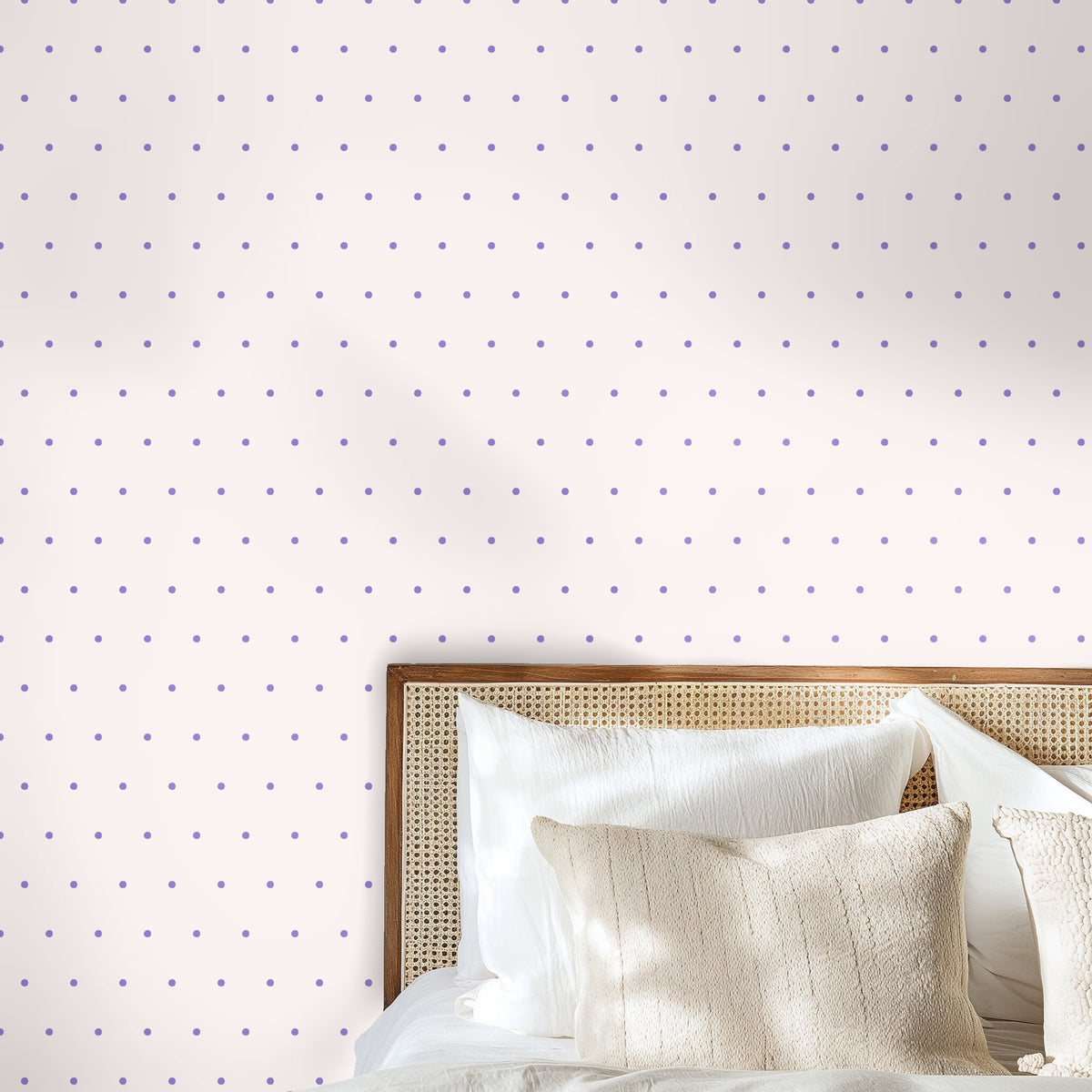 Bedroom vignette with rattan headboard against wallpaper of small lilac dots on a soft blush field