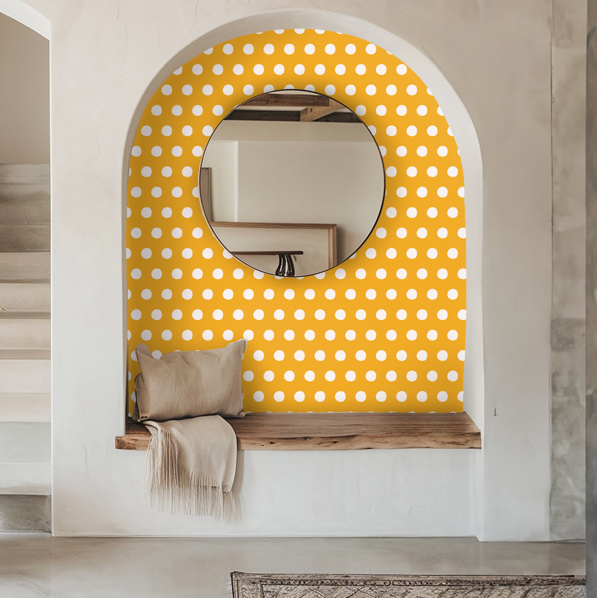 Arched entryway niche lined with marigold polka wallpaper and a round mirror above a wooden bench.