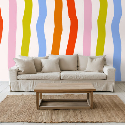Neutral living room sofa against an accent wall with oversized undulating vertical stripes in bright, painterly colors
