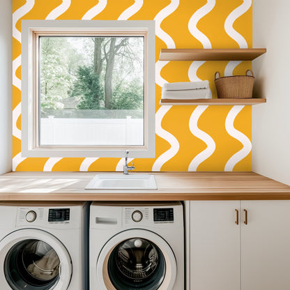 Laundry room countertop and washer beneath a window framed by the bold saffron wave wallpaper
