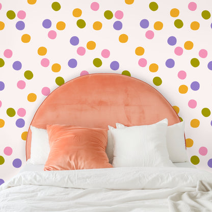 Close-up of wallpaper pattern showing irregular hand-drawn dots in pink, lavender, golden orange and olive on a soft cream background